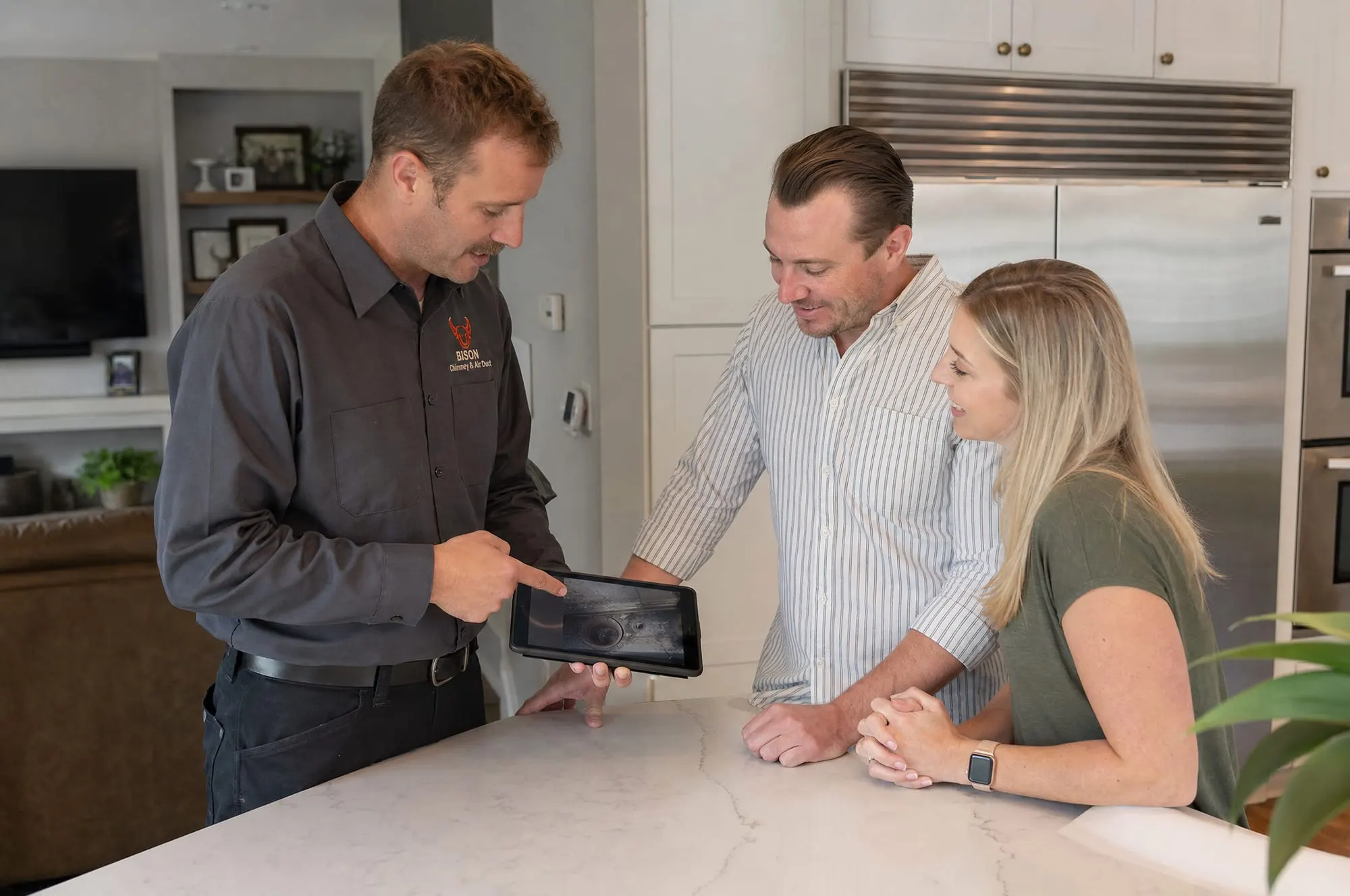 Bison technician showing a homeowner couple chimney inspection photos on a tablet